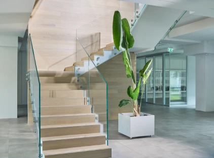 Scala interna in legno e vetro nella sede di Cariaggi, con una pianta ornamentale che esalta l'armonia tra design e natura.