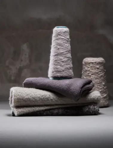 Combinazione di coni di filato e tessuti cashmere esposti in tonalità neutre, simbolo di qualità e stile senza tempo.